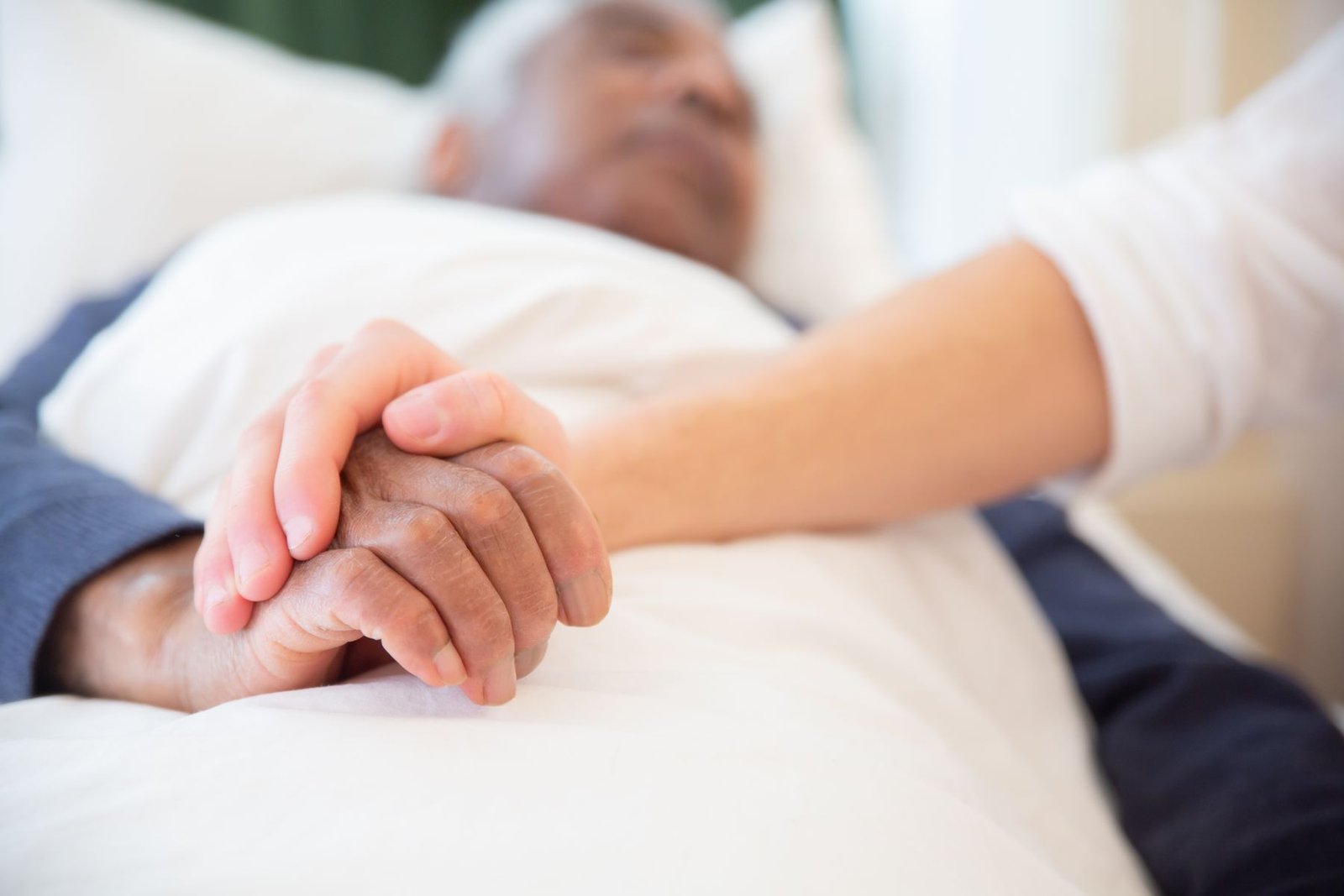 A family member gently holding the hand of a hospice patient